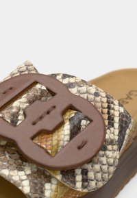 Καφέ σαγιονάρα με σχέδιο φιδιού και μεγάλο ανάγλυφο λογότυπο. Επάνω μέρος από υλικό με υφή και φυσικό χρώμα πάτου. Σόλα με εφέ ξύλου.