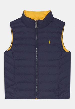 Laivastonsininen puffa-liivi, jossa on korkea kaulus, vetoketjukiinnitys, keltainen vuori ja pieni kirjailtu logo rinnassa. Sileä, tikattu pinta.