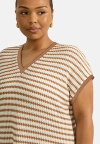 Top lavorato a maglia con uno sfondo crema e strisce verticali marroni, scollatura a V e maniche corte con un bordo marrone a contrasto.