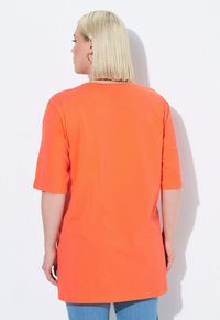 Orange oversized T-shirt with short sleeves and a rounded hem, made of soft fabric. Back view shows a simple design and loose fit.