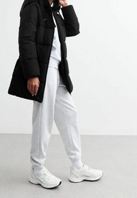 Musta toppatakki hupulla, harmaa puuvillainen collegepaita, harmaat collegehousut ja valkoiset urheilukengät mustilla yksityiskohdilla. Sileä pinta ja rento istuvuus.