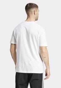 Bílá bavlněná tričko s kulatým výstřihem a krátkými rukávy, pohled zezadu. Zobrazuje hladkou texturu a minimalistický design.