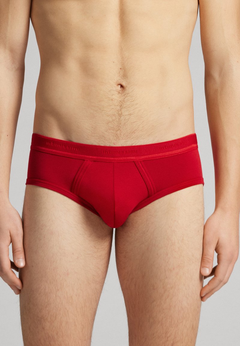 Culotte rouge en coton avec un design ajusté, présentant une poche avant définie, des coutures plates et une taille élastique avec le logo de la marque.
