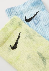 Nike kedu zeķes pasaules zilā un gaiši zaļā krāsā, ar ribota tekstūra un melnu Nike swoosh logotipu uz katras zeķes.