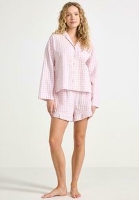 Rosa rutiga bomullspyjamas med en knapp-up topp och shorts med fransad nederkant. Mjuk textur och avslappnad passform för komfort.
