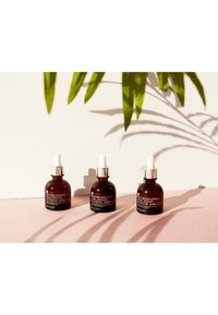 Tres botellas de vidrio ámbar con tapas cuentagotas blancas, etiquetadas como "Ampoule Intensivo Reparador de Caracol", colocadas sobre una superficie rosa.