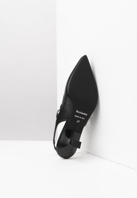 Scarpa con tacco alto in pelle nera, con punta affusolata, lati aperti e un piccolo dettaglio sul tacco. Marcata "NeroGiardini, Made in Italy, 37."