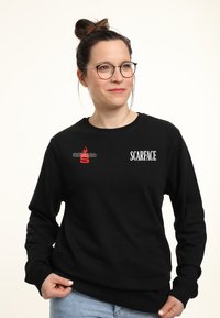 Černá mikina s kulatým výstřihem, se znakem "SCARFACE" a grafikou červeného plamene. Vyrobena z bavlny, hladká textura, volný střih.
