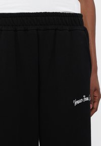 Melni sporta bikses, kas izgatavotas no mīksta auduma ar savelktu jostasvietu, ar baltu izšūtu "Versace Jeans Couture" logo uz kājas.