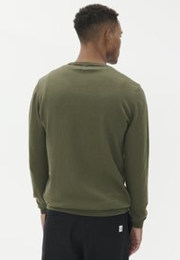 Olivově zelený svetr s dlouhým rukávem, bavlněný materiál, žebrované manžety a lem, kulatý výstřih, obsahuje štítek na dolní pravé straně.