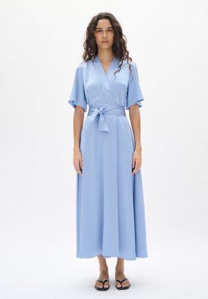 Light blue wrap dress with short flutter sleeves, a tied belt, and floor-length skirt in a soft, textured fabric. Sandals visible at the bottom.