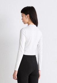 White long-sleeve top with a round neckline, made of soft material, paired with black high-waisted leggings. Minimalist design, fitted silhouette.