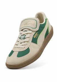 Puma-sneakers med en beige ruskindsoverdel og grønne detaljer, en polstret krave, perforerede sidelæger og en struktureret brun gummisål.