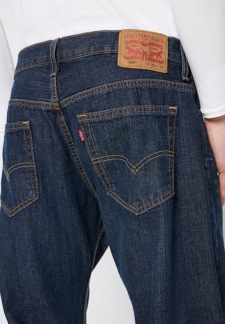 Jean en denim bleu foncé avec une coupe droite, arborant une patch en cuir étiqueté "Levi Strauss & Co.", et un piqûre distinctive sur les poches arrière.
