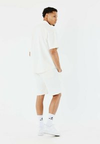 Lichtgekleurde polo met korte mouwen, gecombineerd met bijpassende shorts. De outfit heeft een zachte textuur, een casual pasvorm, en witte sneakers met branding.