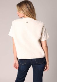 Gilet en fausse fourrure crème au fit ample, avec un col arrondi et un petit logo dans le dos. Associé à un jean en denim foncé.