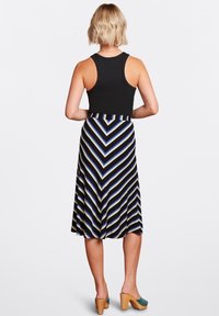 Černý žebrovaný tílko spojený s dlouhou sukní s chevronovým vzorem v černé, modré a žluté pruhy, doplněné botami na blokovém podpatku.