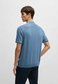 Ljusblå kortärmad pikétröja med texturerad finish, vikta ärmslut och krage. Sömmar längs axlarna och ryggen.