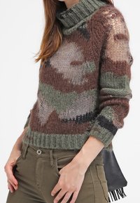 Neulepaita, jossa on korkea poolokaulus, monivärinen naamiointi maanläheisissä sävyissä, ribbireunat hihoissa ja helmassa, ja löysä istuvuus.