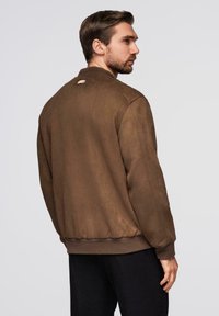 Ruskea tekonahkainen bomber-takki, jossa on ribbed-mansetit ja helma, pieni brändilogo selässä ja rento malli.