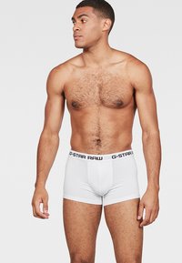 Boxer da uomo bianchi con una cintura nera con logo. Realizzati in tessuto liscio, presentano un design aderente e una lunghezza delle gambe corta.