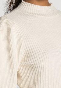 Kremowy sweter z golfem, zrobiony z miękkiej dzianiny. Posiada dopasowany krój i teksturowane pionowe linie wzdłuż rękawów.