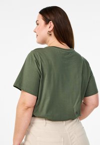 Oliven grøn kortærmet T-shirt med rund hals, lavet af blødt materiale. Stylet med cremede bukser, der viser en afslappet pasform.