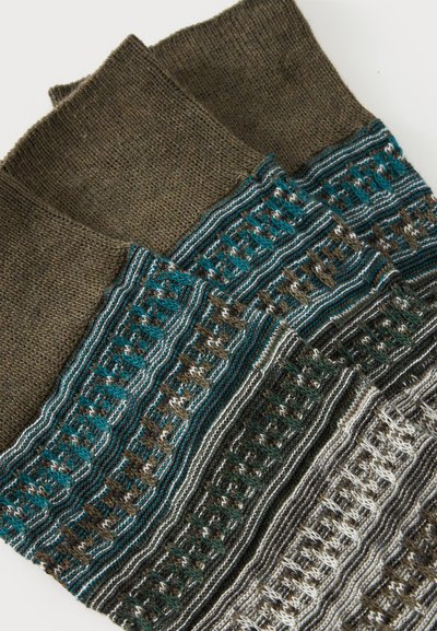 Trois chaussettes épaisses en tricot pliées avec des rayures à motifs vertes, marron, blanches et bleu sarcelle sur un fond blanc.