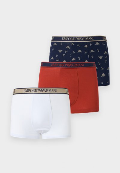 Τρία ανδρικά boxer Emporio Armani: λευκά, κόκκινα και ναυτικό μπλε με μοτίβο λογοτύπου, το καθένα με λουράκια μέσης με το λογότυπο στα αντίστοιχα χρώματα.