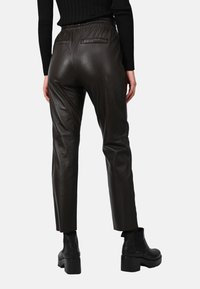 Hnědé kožené kalhoty s hladkým povrchem, elastickým pasem a zadními kapsami. V kombinaci s černými botami na podpatku, pohled zezadu.