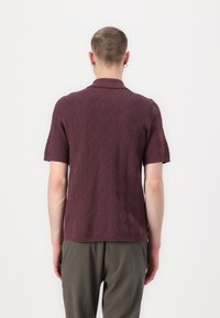 Burgundská polo košeľa s krátkym rukávom, ktorá má textúrovaný cik-cak vzor. Vyrobená z pleteného materiálu, má klasický golier a rebrovaný lem.