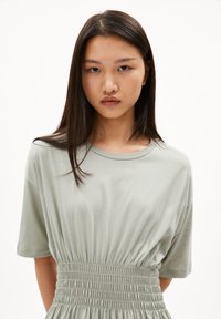 Light green short-sleeve shirt with a relaxed fit and gathered waistband. Smooth cotton fabric with a soft texture.