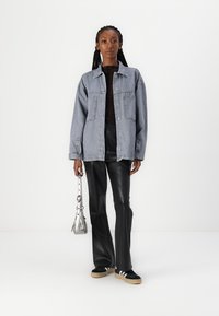 Giubbotto di denim azzurro chiaro con due tasche frontali, abbinato a pantaloni in pelle nera e sneaker nere con strisce bianche. Borsa argentata.