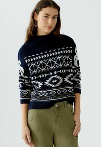 Navy trui met witte en blauwe geometrische patronen, ronde hals en lange mouwen, gecombineerd met olijfgroene broek.
