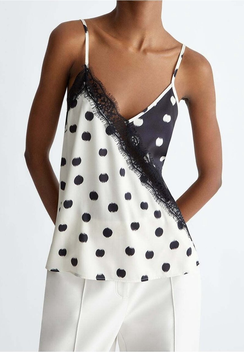 Camisole en satin noir et blanc avec une fente diagonale ornée de grands pois, bordure en dentelle le long de l'encolure et fines bretelles réglables.