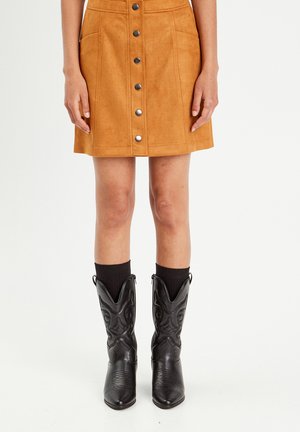 Tan suede skirt with a-line shape, front button closure, and two pockets. Paired with black cowboy boots and ribbed black socks.