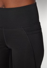 Højtaljede sorte leggings lavet af strækstof, med glat tekstur, syningsdetaljer og en lille sidelomme.