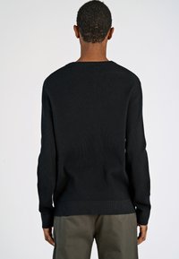 Schwarzer gerippter Pullover mit langen Ärmeln und rundem Halsausschnitt, ausgestattet mit einem strukturierten Strickmuster und einer leicht lockeren Passform an der Taille.
