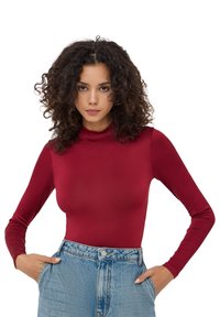 Body rosso a maniche lunghe con collo alto finto realizzato in un tessuto liscio e elasticizzato. Abbinato a jeans in denim azzurro chiaro a vita alta con vestibilità classica.