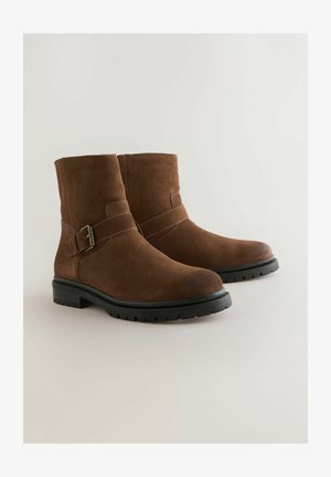 Brown suede ankle boots with black rubber soles and buckle straps, shown side by side on a light background.