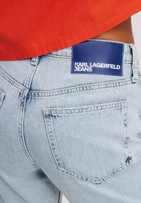 Lichtblauwe denim jeans met een opvallende blauwe leren patch op de achterkant, met witte tekst "KARL LAGERFELD JEANS." Eenvoudig ontwerp.