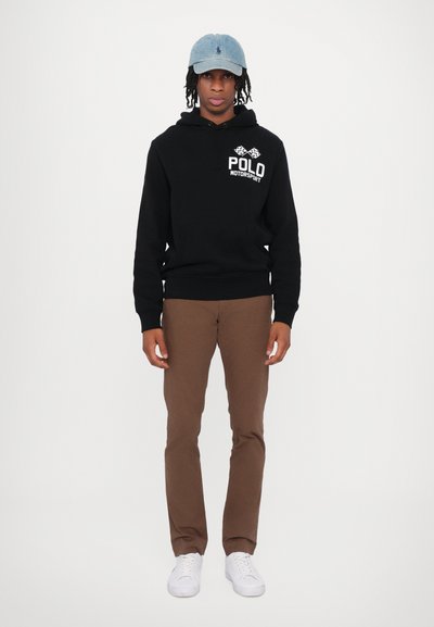 Melna kapuce ar baltu "POLO MOTORSPORT" logotipu, brūnas bikses un baltas kedas. Denima cepure noslēdz ikdienišķo apģērbu. Gludas tekstūras.