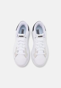 Valged lukked tenistosidemed, millel on sile nahk ülemine osa, beežid külgaktsendid, must kannatugi ja tekstureeritud kummitald. PUMA logo keeles.