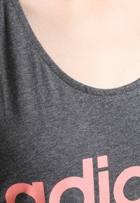 Close-up van de nek en bovenborst die een donkergrijs T-shirt draagt met een gedeeltelijk zichtbaar roze kleine letters logo.