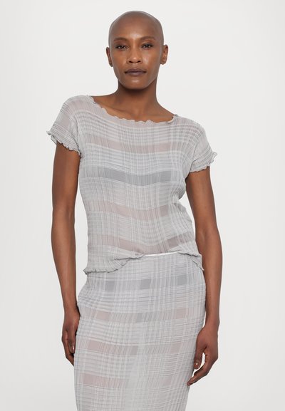 Blusa grigia trasparente con un motivo a quadri testurizzato, scollatura arrotondata e maniche a volant. Il tessuto aderisce dolcemente alla figura.