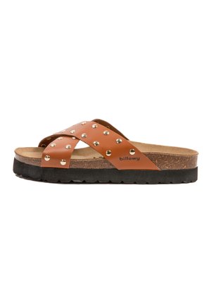 Sandale en cuir marron avec deux brides croisées ornées de clous en argent, une semelle en liège et une semelle en caoutchouc noire.