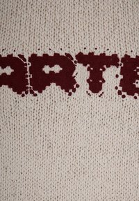 Tessuto lavorato a maglia di colore crema con grandi testi color amaranto. La trama è spessa, mostrando un motivo a maglia stretta con alcuni fili sciolti.