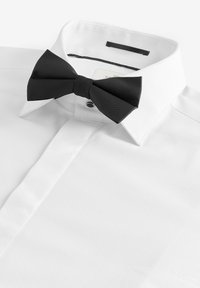 Camicia bianca in tessuto testurizzato, con papillon nero a coste. Collo classico e chiusura con un solo bottone visibile.
