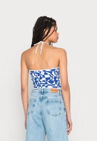 Top cropped azul com padrão, com amarração no pescoço e detalhes brancos, combinado com jeans de cintura alta azul clara, com um rótulo na parte de trás.