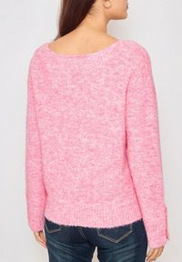 Pull en tricot rose, à coupe décontractée, avec un grand décolleté au dos, des manches longues et une finition légèrement texturée. L'ourlet est légèrement plus long à l'arrière.